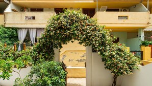 A courtyard with a central archway covered in flowering plants, surrounded by buildings with balconies and windows. - Apartment Iris by Interhome (Villasimius)
