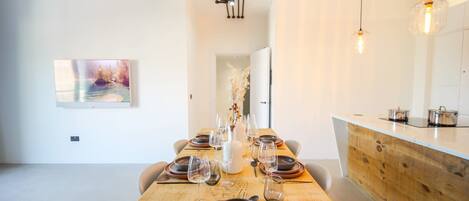 A modern dining area with a wooden table set for a meal, a white vase centerpiece, and pendant lighting.