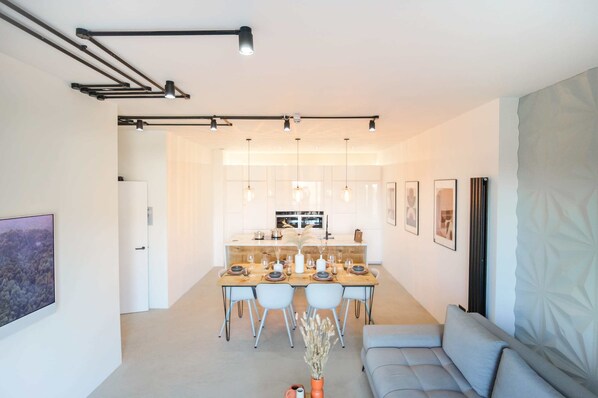 A modern kitchen with a central island, pendant lighting, and a dining area with a sofa and chairs.