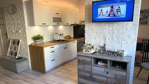 A modern kitchen with white cabinets, a wooden countertop, and a built-in dishwasher. A flat-screen TV is mounted on the wall above the counter. - Apartment in Gdańsk near Brzeźno Pier (Gdańsk Brzeźno)