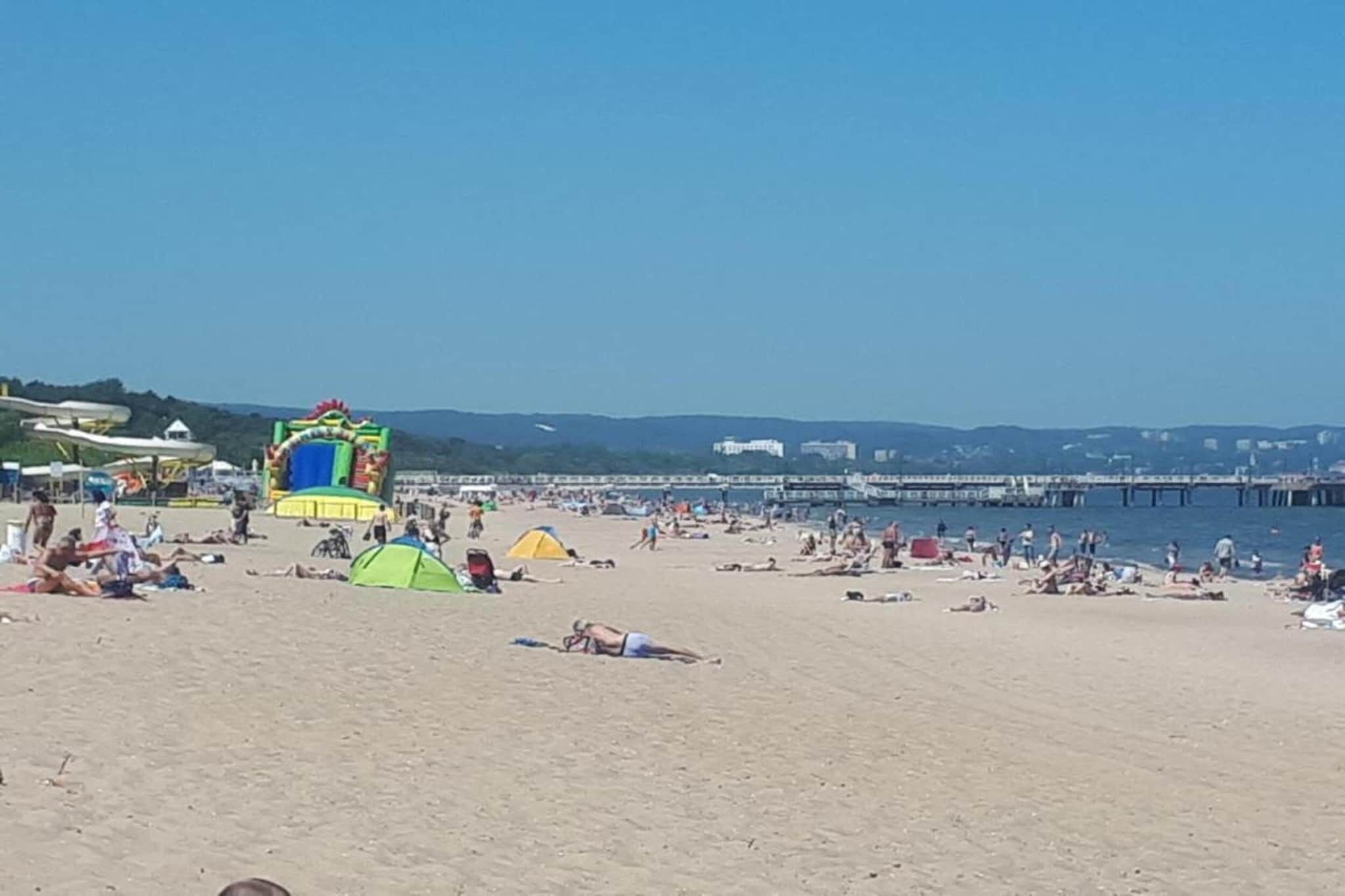 En strand med tält, en vattenrutschkana och en brygga i bakgrunden.