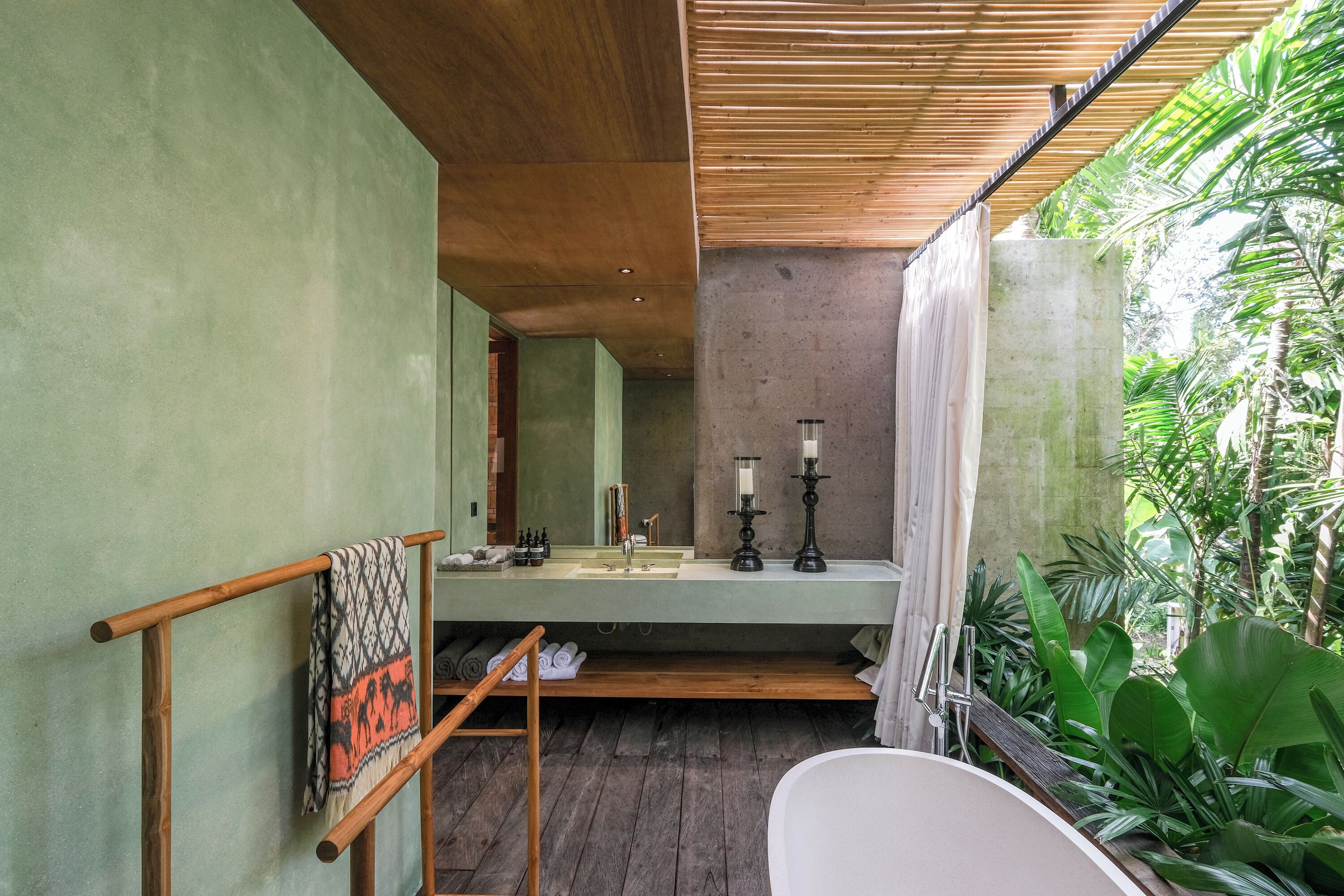 A bathroom with a wooden ceiling, a bathtub, a sink with candles, and a towel rack.