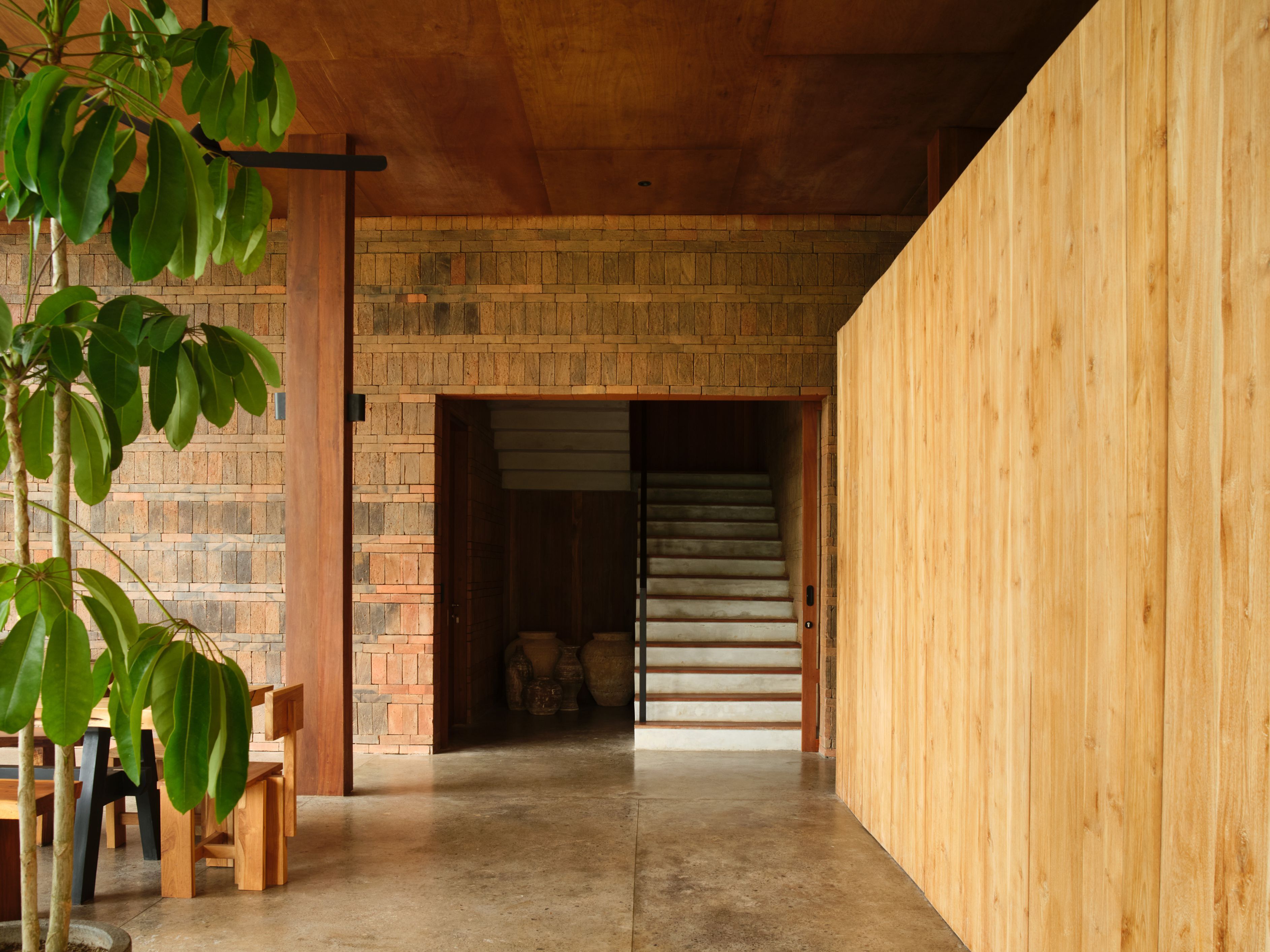 A hallway with a wooden floor, brick walls, and a staircase leading to a room.