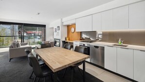 A modern kitchen with white cabinets, a wooden dining table, and a built-in oven. - Modern Apartment Near Coronet Peak Ski Field (Queenstown)