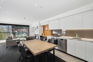 A modern kitchen with white cabinets, a wooden dining table, and a built-in oven.