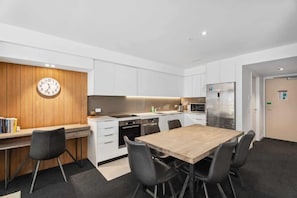 Cocina moderna con armarios blancos, un reloj de pared de madera, una mesa de comedor con sillas y un refrigerador.