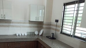 A kitchen with wooden cabinets, a granite countertop, and a window with blinds. - Soni Homestays (Khalilabad)
