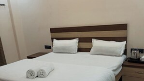 A neatly made bed with white linens and pillows, a wooden headboard, a bedside table with a kettle, and a small drawer unit. - Soni Homestays (Khalilabad)