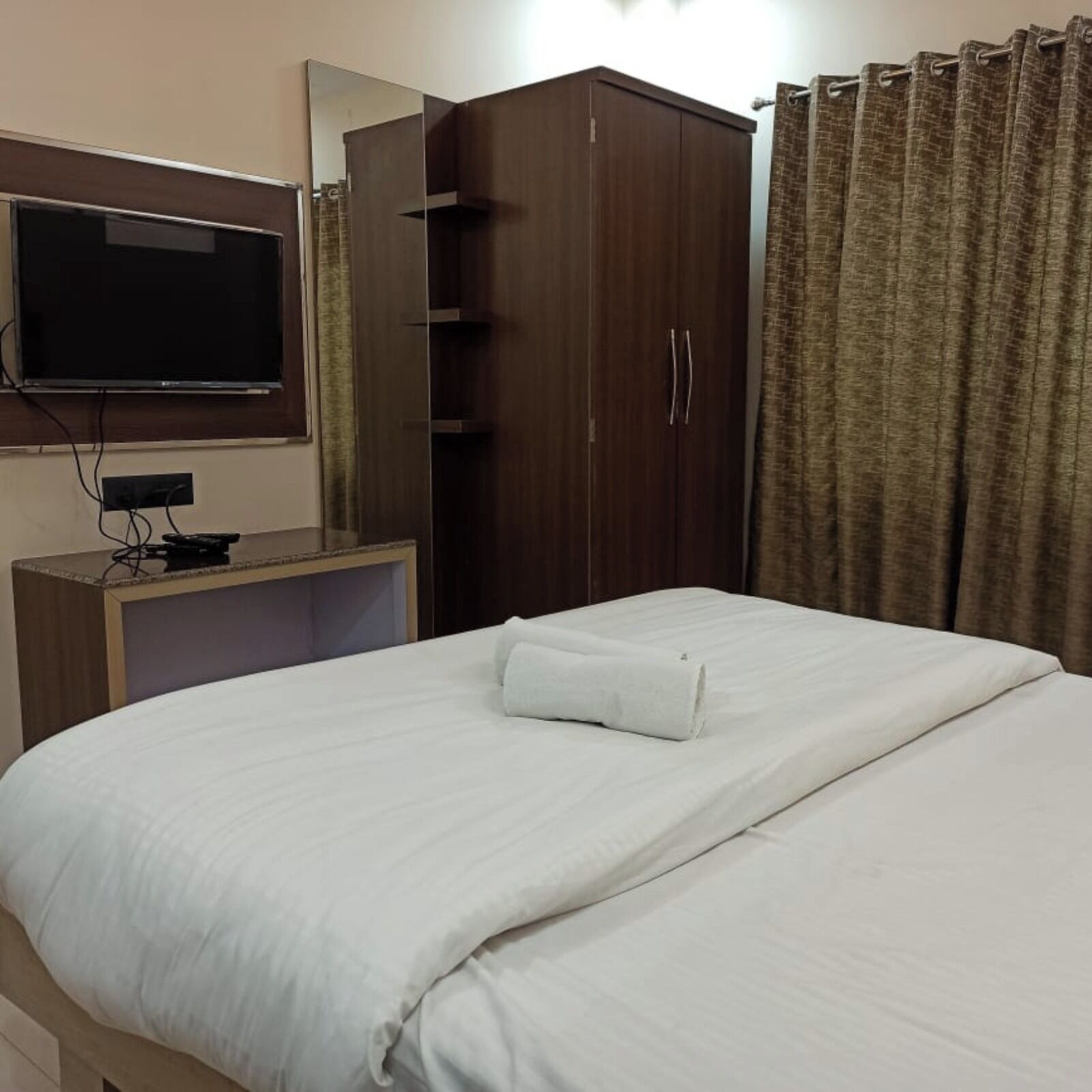 A hotel room with a bed, a TV mounted on the wall, a wardrobe, and a curtain.