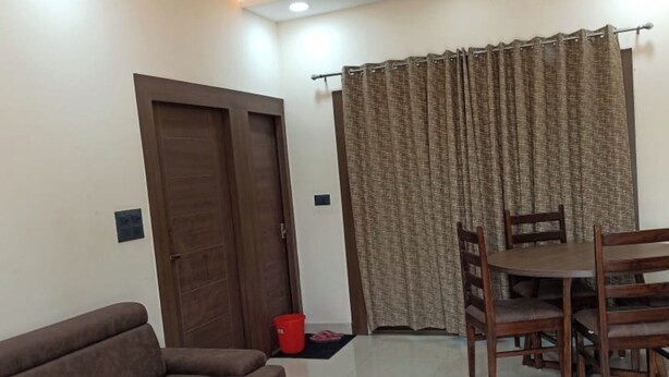 A living room with a sofa, a glass coffee table, a dining table with chairs, a ceiling fan, and curtains. - Soni Homestays (Khalilabad)