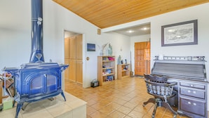 Una habitación con un estufa de leña azul, armarios de madera, una silla y un piano.