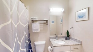 Une salle de bain avec un rideau de douche, des toilettes, un lavabo avec un miroir et un tableau encadré au mur.