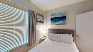 A hotel room with a bed, a nightstand, a lamp, a window with blinds, and two wall art pieces. - RD102 - Home|Yard|12mi to Convention Ctr|Sleeps 6 (Richardson)