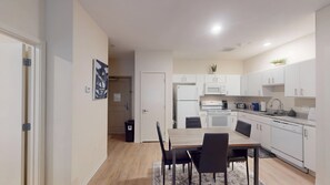 A modern kitchen with white cabinets, a microwave, stove, and a sink. There is a dining table with chairs and a small rug.