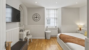 Ein Schlafzimmer mit Bett, Schreibtisch, Stuhl, Wanduhr, Fenster und Heizkörper.
