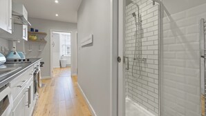 Eine moderne Küche mit Holzboden, einer gläsernen Dusche und Blick auf einen Flur.