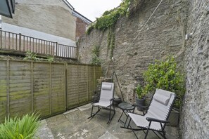 A small outdoor seating area with two chairs and a table, a wooden fence, and a stone wall. - Apartment in Grade II Listed Building, Dartmouth (Devon)