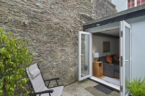 A modern room with a grey sofa, a small wooden side table, and a door leading outside. - Apartment in Grade II Listed Building, Dartmouth (Devon)