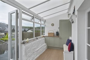 Un invernadero con vistas a casas, suelo de madera, pared blanca y ventana con marco blanco.