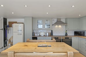 Una cocina moderna con armarios blancos, una mesa de comedor de madera y electrodomésticos integrados.