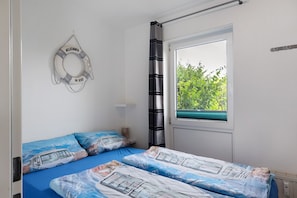 A bedroom with a bed, a window, curtains, a wall-mounted life preserver, and a view of greenery outside.