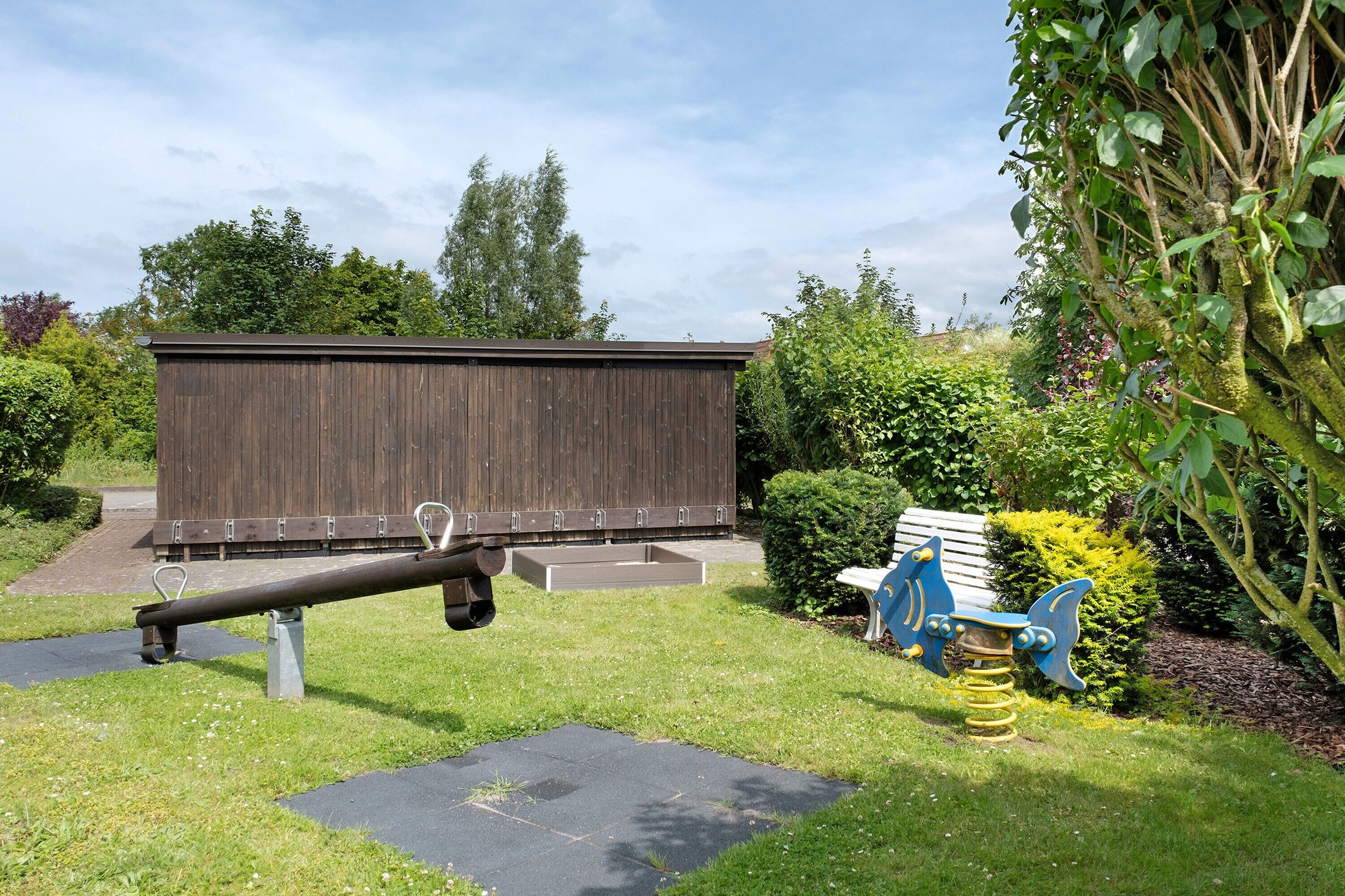 Ein Spielplatz mit Wippe, Schaukel und einer Holzkonstruktion in einem Garten.