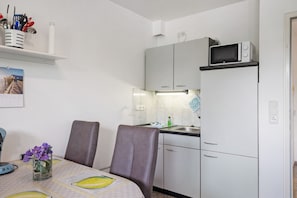 A compact kitchen with a microwave, sink, and cabinets. There is a dining table with chairs and a vase of flowers.