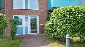 A brick building with a blue door and window, a paved entrance, and a well-maintained hedge.