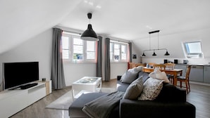 A modern living room with a flat-screen TV, a sofa, a coffee table, and a dining area with a table and chairs. - Apartment 'Ferienwohnung Windrose' with Private Terrace and Wi-Fi (Pellworm)