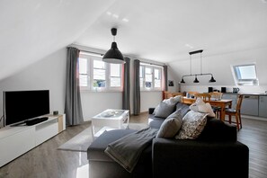 Un soggiorno moderno con una TV a schermo piatto, un divano, un tavolino da caffè e un'area pranzo con tavolo e sedie.