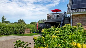 A building with a wooden deck, a red umbrella, and solar panels. - Apartment 'Ferienwohnung Windrose' with Private Terrace and Wi-Fi (Pellworm)