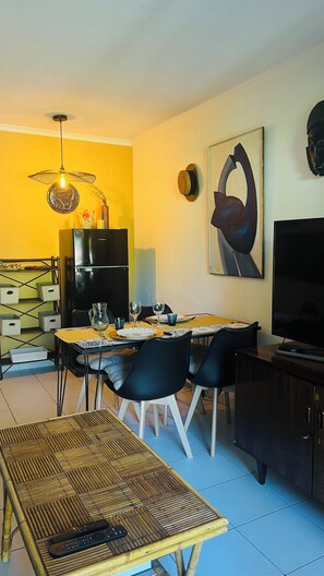 A dining area with a table set for four, a black refrigerator, a TV, and a painting on the wall.