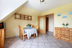 Uma área de refeições com mesa, cadeiras, um armário e uma prateleira com objetos.