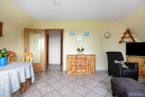 Uma sala de estar com um armário de madeira, uma televisão, um sofá e uma mesa de jantar com cadeiras.