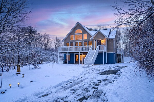 A two-story house with a balcony, a staircase, and a driveway covered in snow.