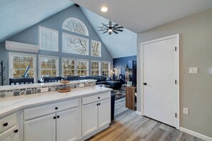 A modern kitchen with white cabinetry, a marble countertop, and a large window with multiple panes.
