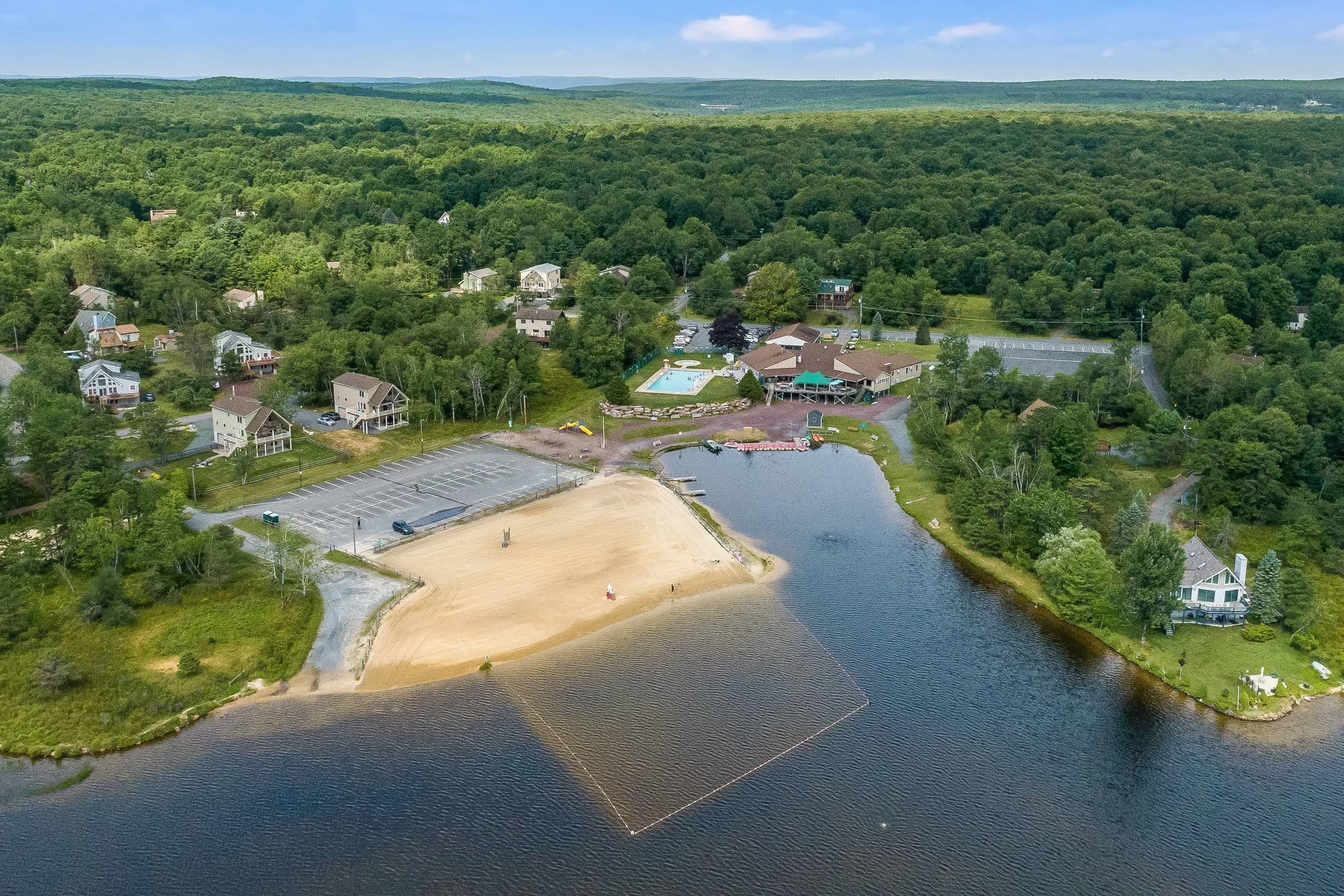 An aerial view of a lakeside community with houses, a swimming pool, and a sandy beach area.