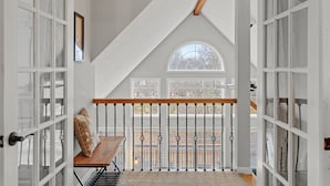 A room with a sloped ceiling, a wooden bench, a view through a window, and a white door with glass panels. - Hot Tub, Game Room, Dog Friendly, Sports Bar, A/C (Albrightsville)