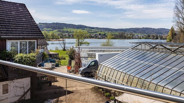 A house with a greenhouse, a truck, and a river in the background.