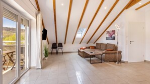 A spacious room with a large sliding glass door, a sofa set, a coffee table, and a ceiling with exposed wooden beams.