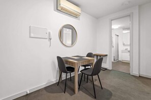A room with a dining table, four chairs, a round mirror, an air conditioning unit, and a white wall.