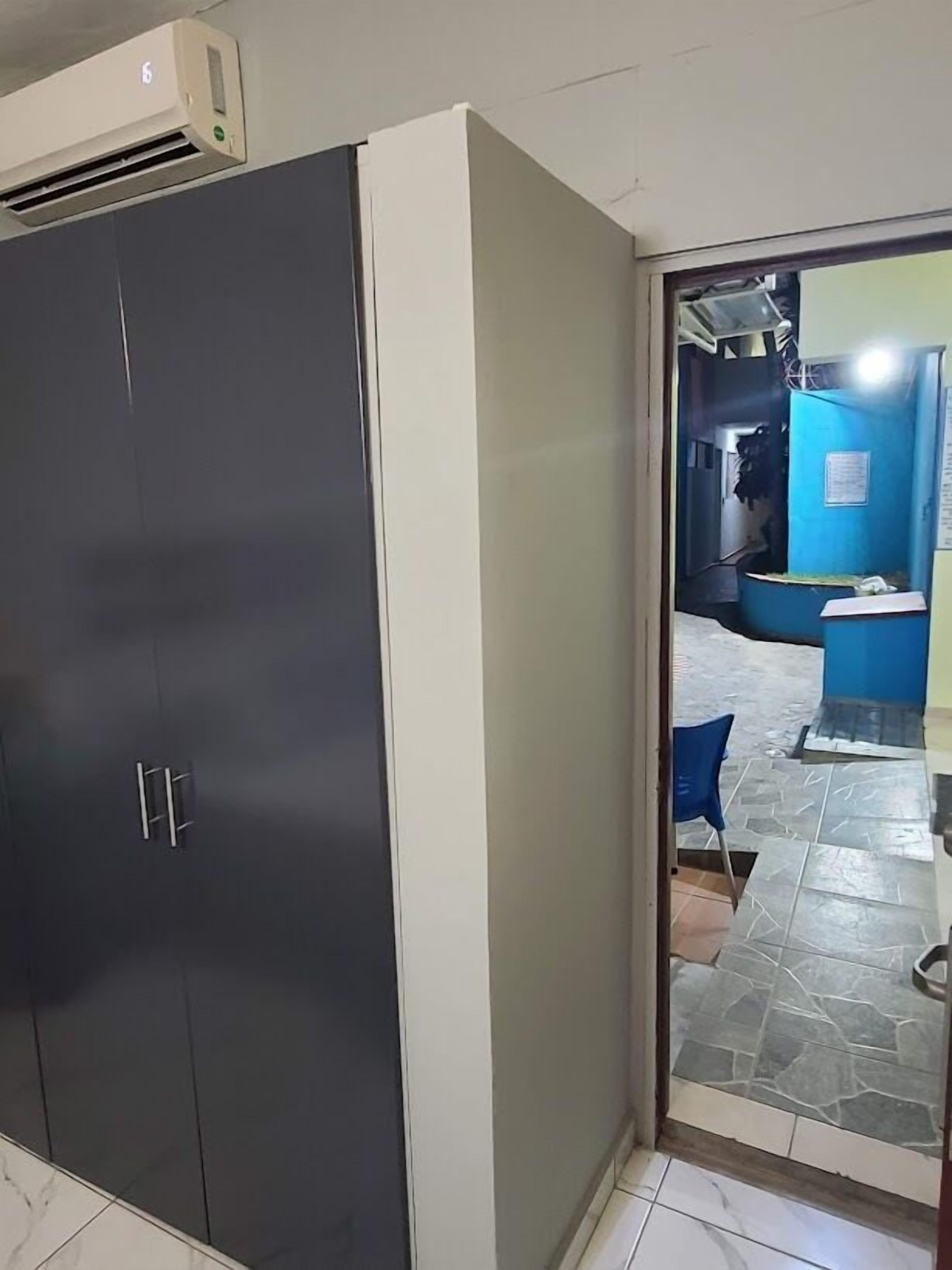 A room with a large wardrobe, a tiled floor, and a doorway leading to a bathroom with a blue wall and a sink.
