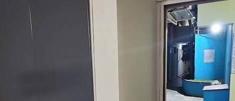 A room with a large wardrobe, a tiled floor, and a doorway leading to a bathroom with a blue wall and a sink.