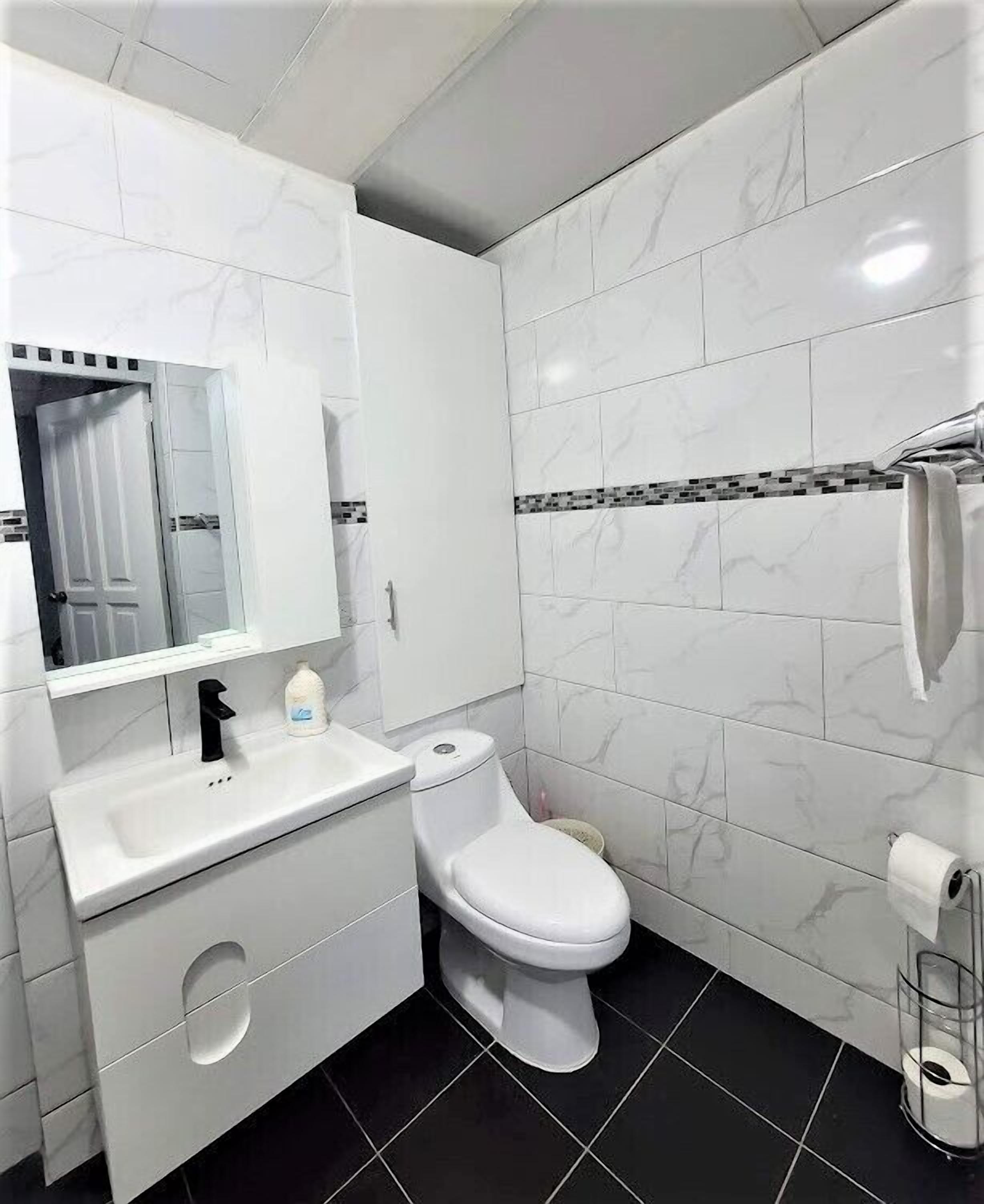 A modern bathroom with white marble tiles, a white sink with a black faucet, a white toilet, and a glass shower enclosure.