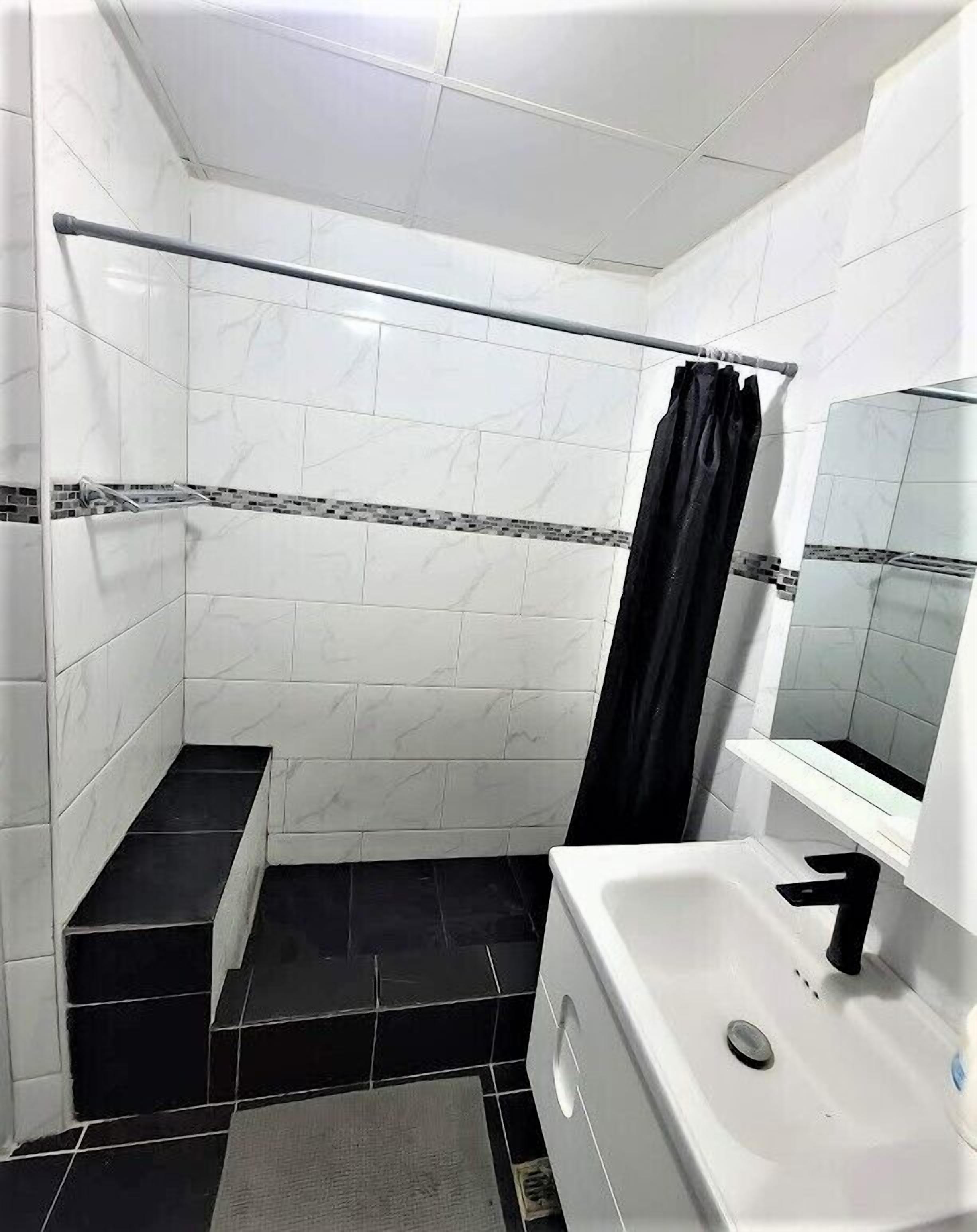 A small, modern bathroom with white and black tiles, a black shower curtain, and a white sink with a mirror.