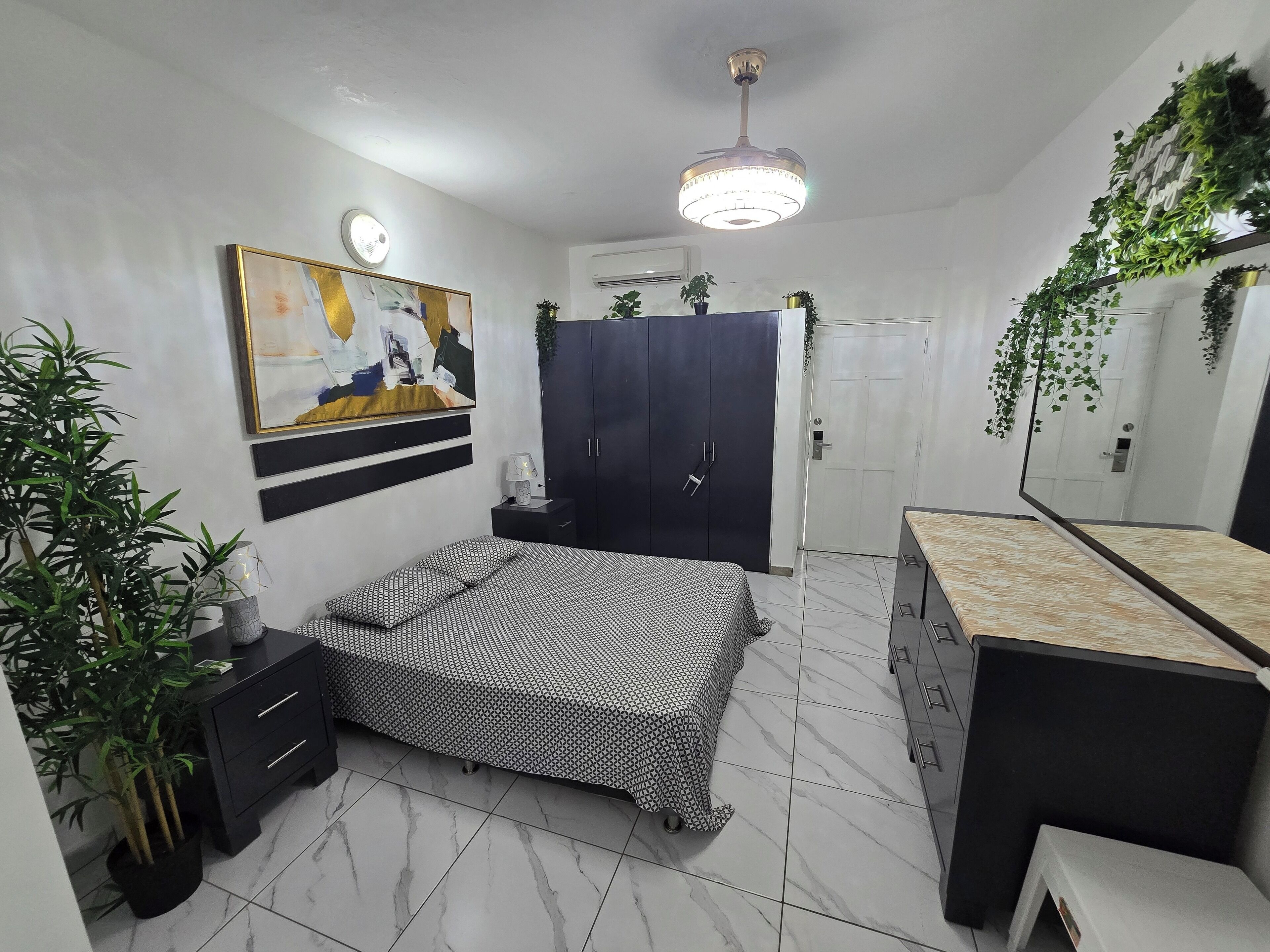 Un dormitorio con una cama, un armario, una mesita de noche, un espejo y una planta colgante.