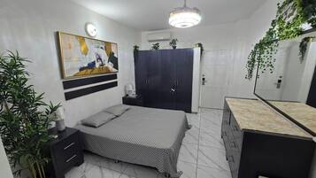 Une chambre à coucher comprenant un lit, une armoire, une table de chevet, un miroir et une plante suspendue.