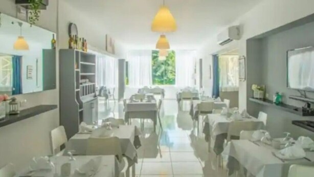 Een restaurant met witte tafels en stoelen, gele hanglampen en uitzicht op groen.