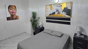 Een slaapkamer met een bed, nachtkastje, lamp, een schilderij aan de muur en een plafondlamp.