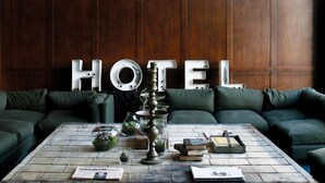 Un hall d’hôtel accueillant, avec un grand mur en bois, un ensemble de canapés verts et une table basse agrémentée de livres et d’objets décoratifs.